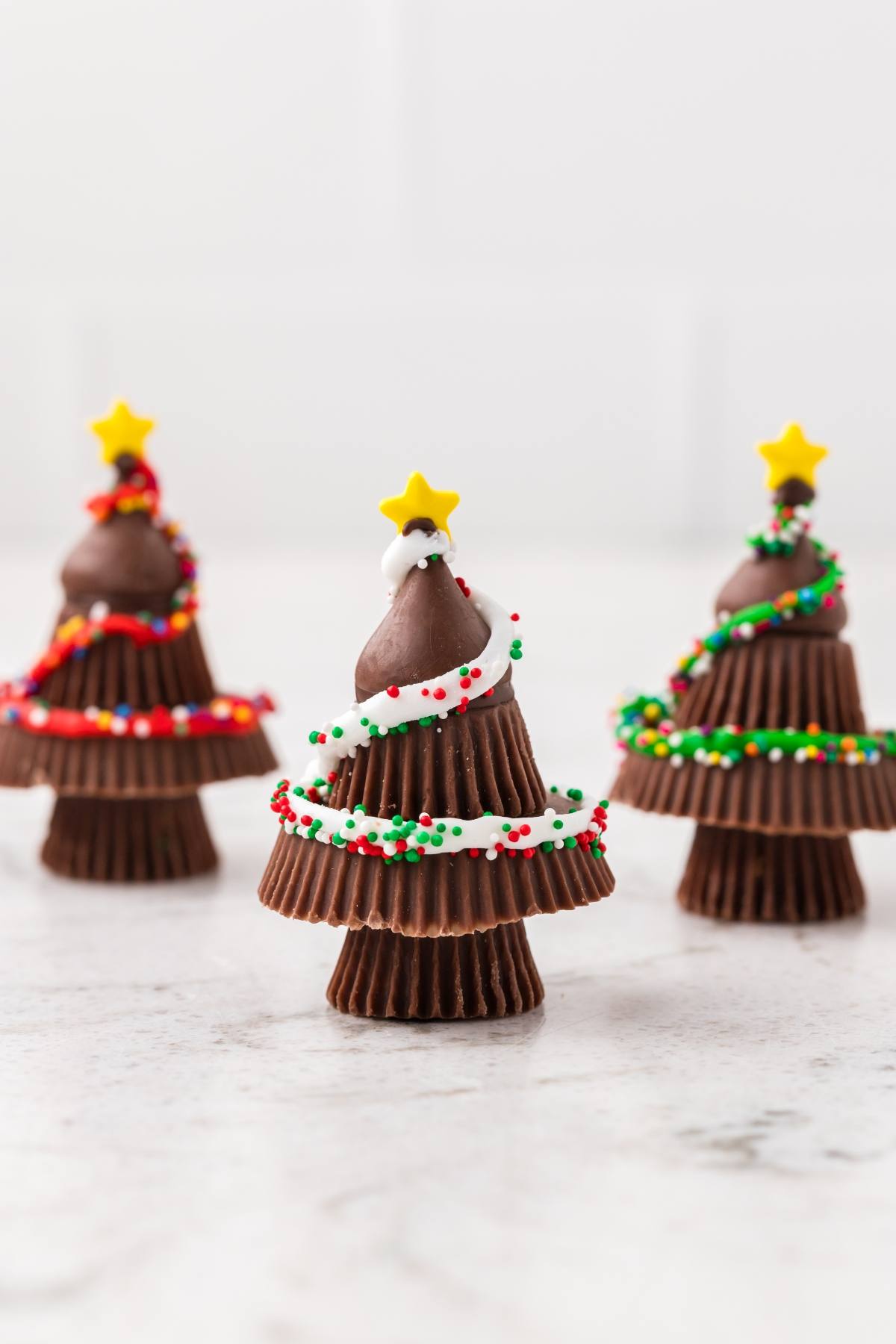 Chocolate Christmas tree treats made from peanut butter cups and kisses, decorated with icing, sprinkles, and stars.