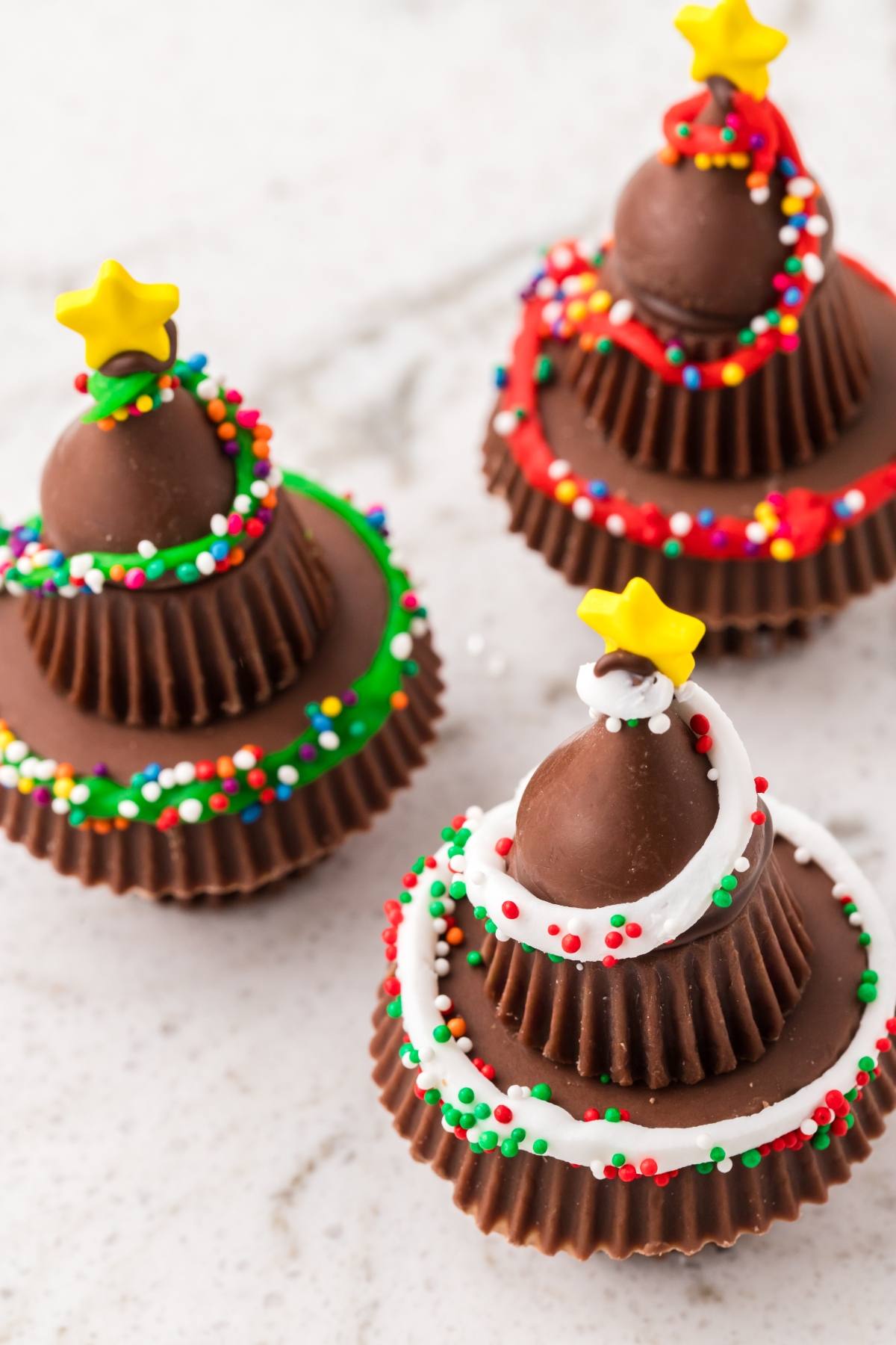 Three stacked chocolate peanut butter cups decorated as Christmas trees with colorful icing and sprinkles.