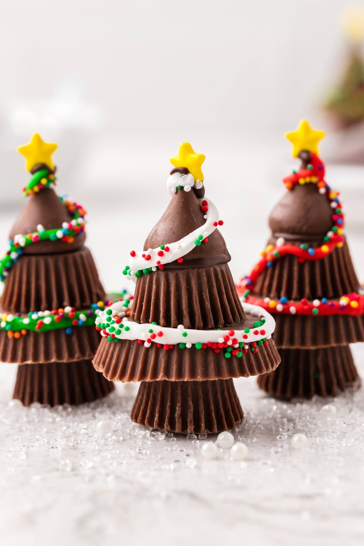 Three Christmas tree-shaped treats made from stacked chocolate cups, icing, sprinkles, and star toppers.