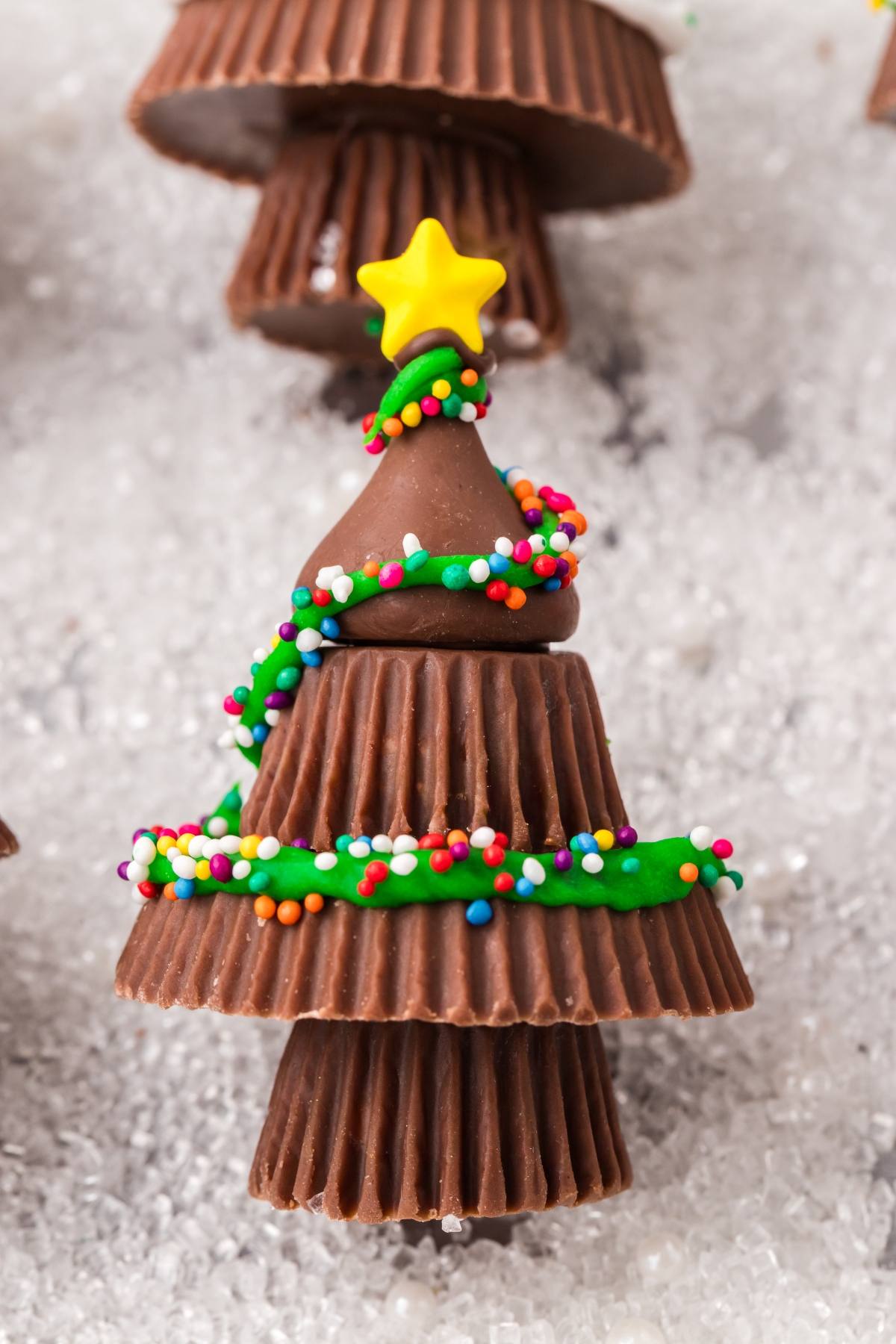 Chocolate Christmas tree made of peanut butter cups, topped with a yellow star and decorated with green icing and sprinkles.