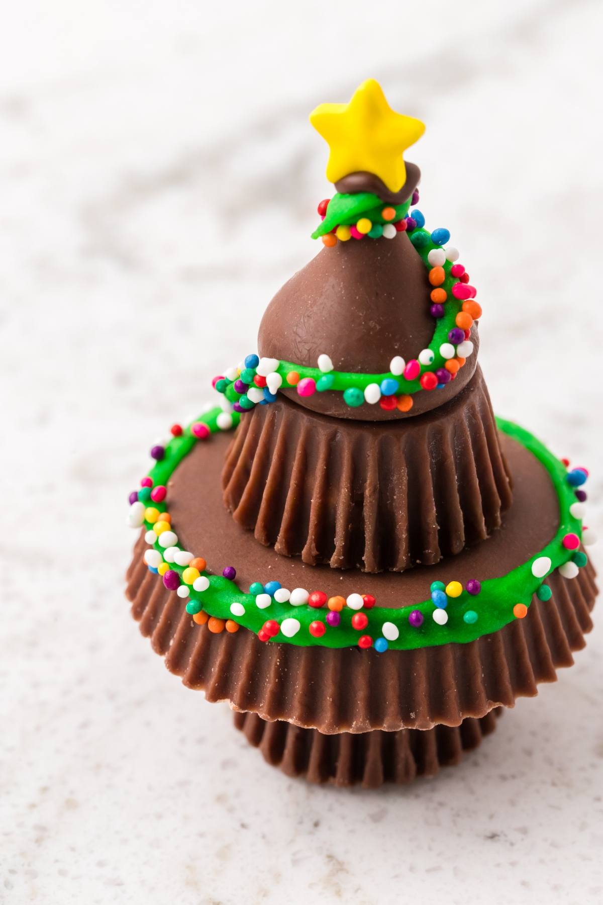 Three stacked chocolate peanut butter cups decorated as a Christmas tree with green icing, sprinkles, and a star.