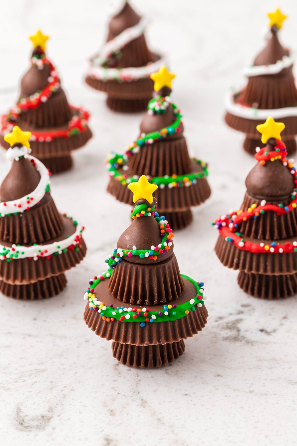 Chocolate Christmas tree treats made from stacked candies, decorated with icing, sprinkles, and yellow star toppers.