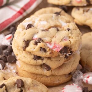 A stack of Peppermint Chocolate Chip Cookies with peppermint pieces, surrounded by chocolate chips and festive peppermint candies.