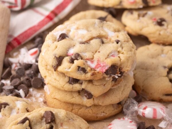 A stack of Peppermint Chocolate Chip Cookies with peppermint pieces, surrounded by chocolate chips and festive peppermint candies.