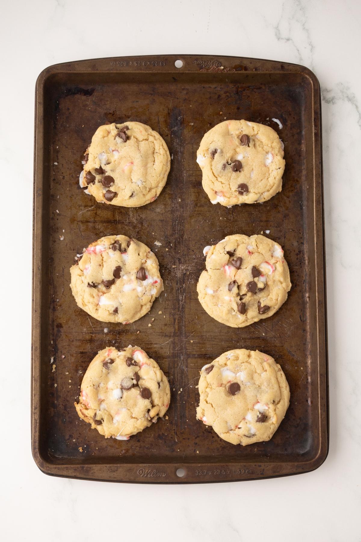 Six chocolate peppermint chip cookies on a dark baking sheet, resting on a white marble surface.