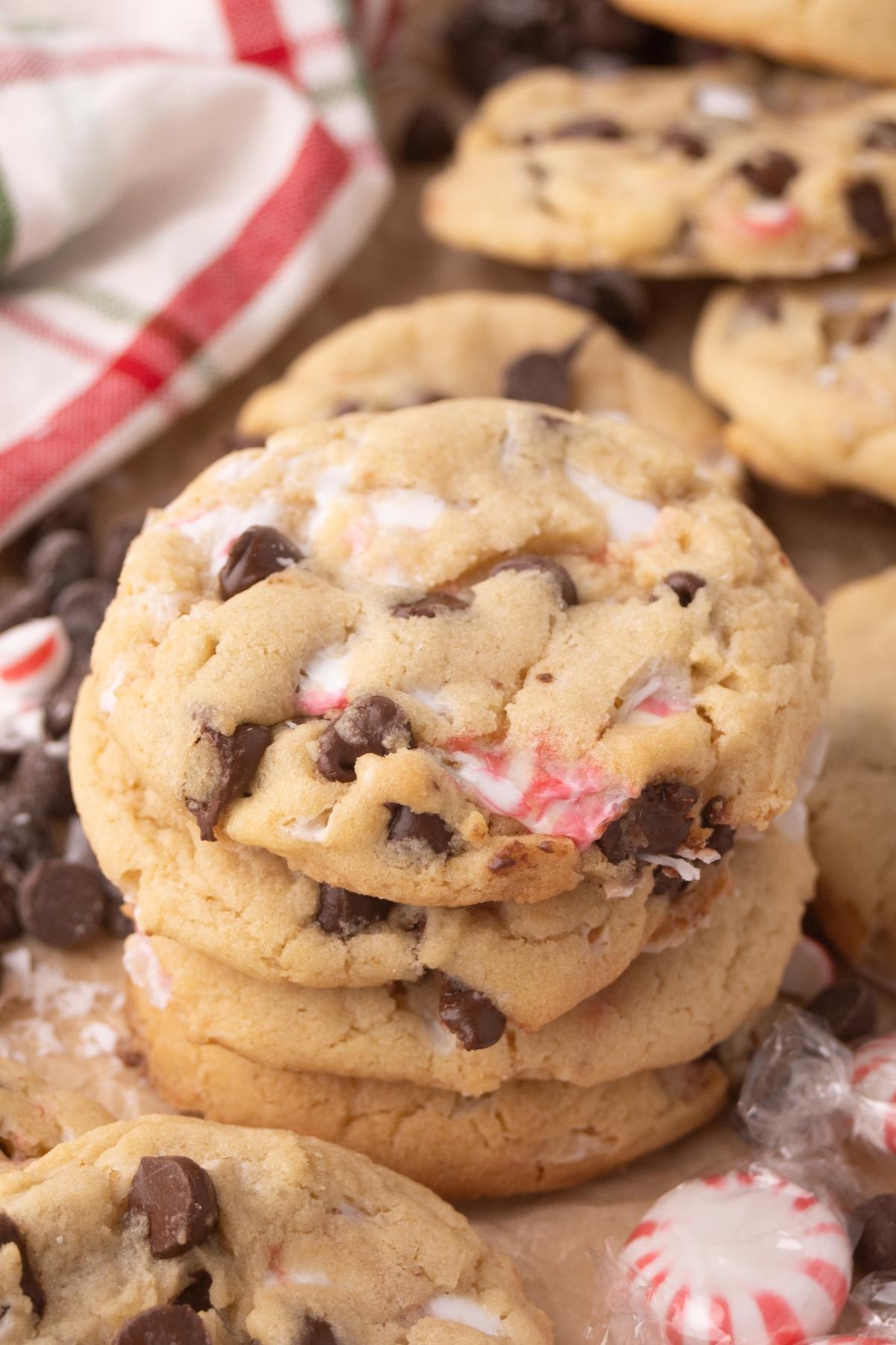 A stack of peppermint chocolate chip cookies with crushed peppermint candies, on a brown surface near a red and green towel.
