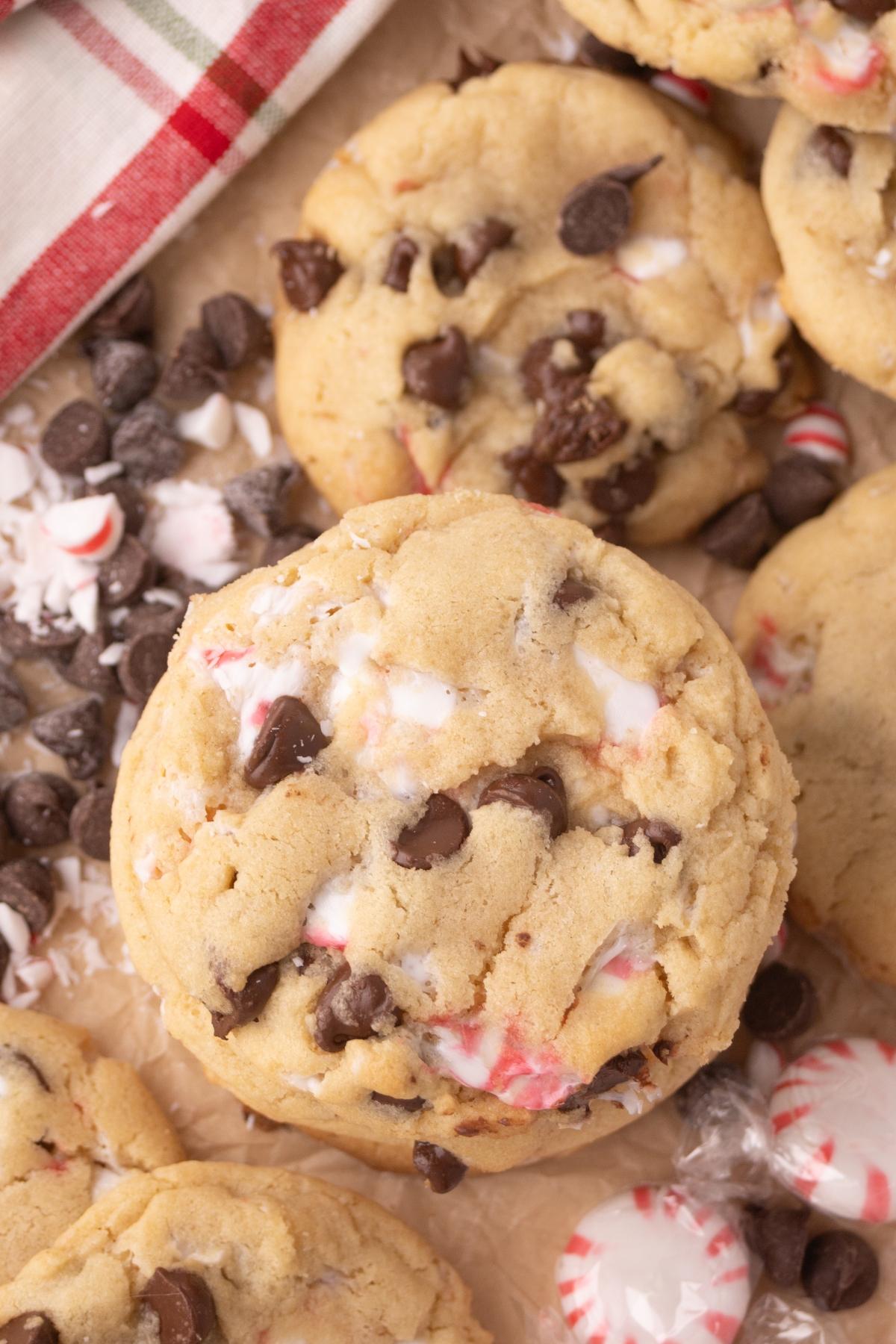 peppermint Chocolate chip cookies with crushed peppermint pieces on parchment paper, surrounded by chocolate chips and mints.