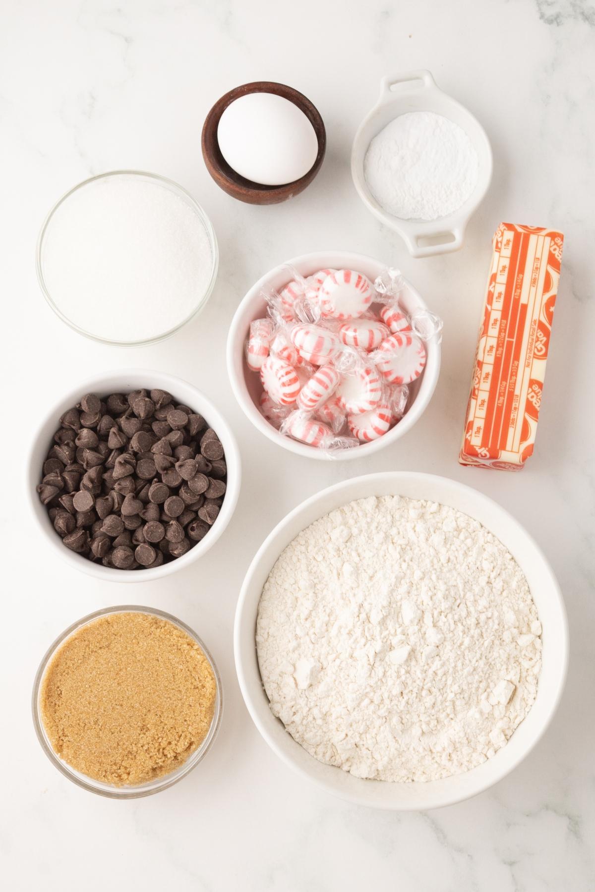 Baking ingredients: flour, sugar, brown sugar, egg, butter, baking soda, chocolate chips, and peppermint candies.