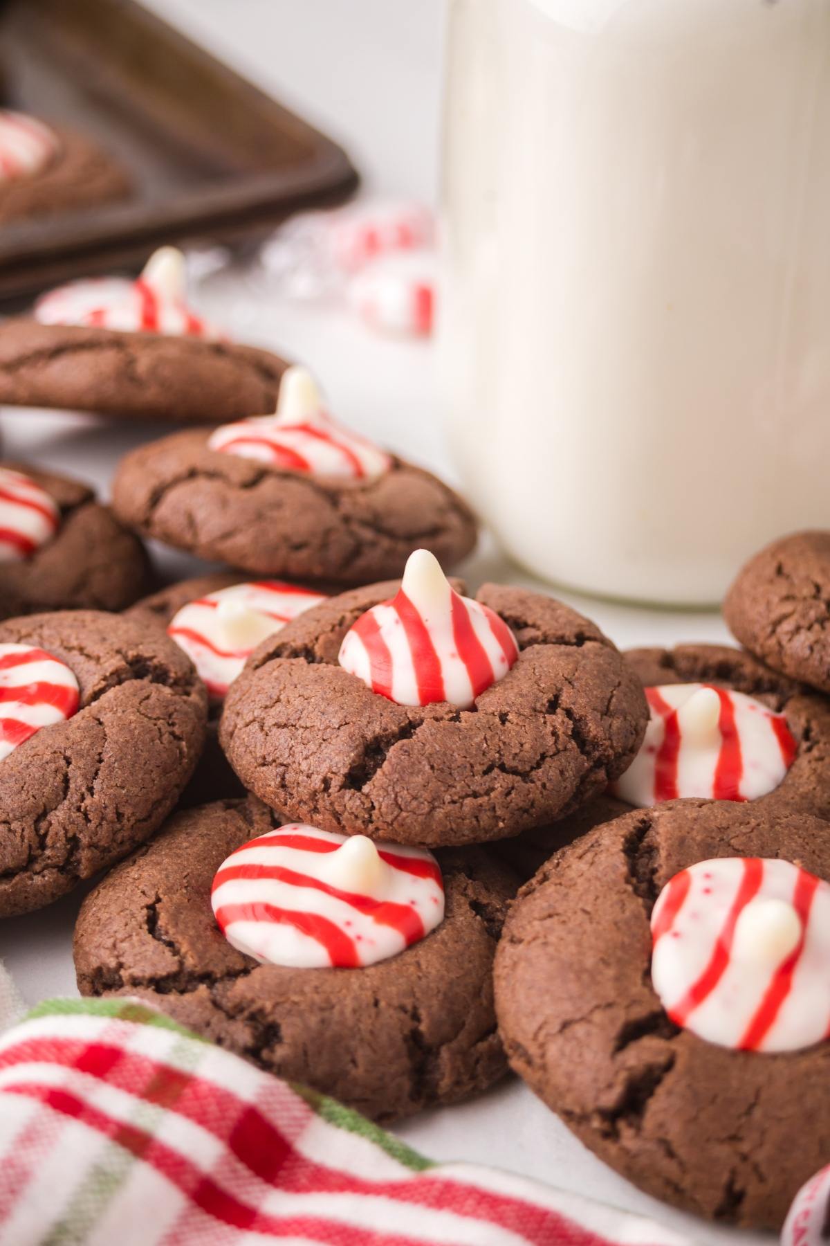 Chocolate Peppermint kiss cookies with red and white striped peppermint candies on top, next to a glass of milk.