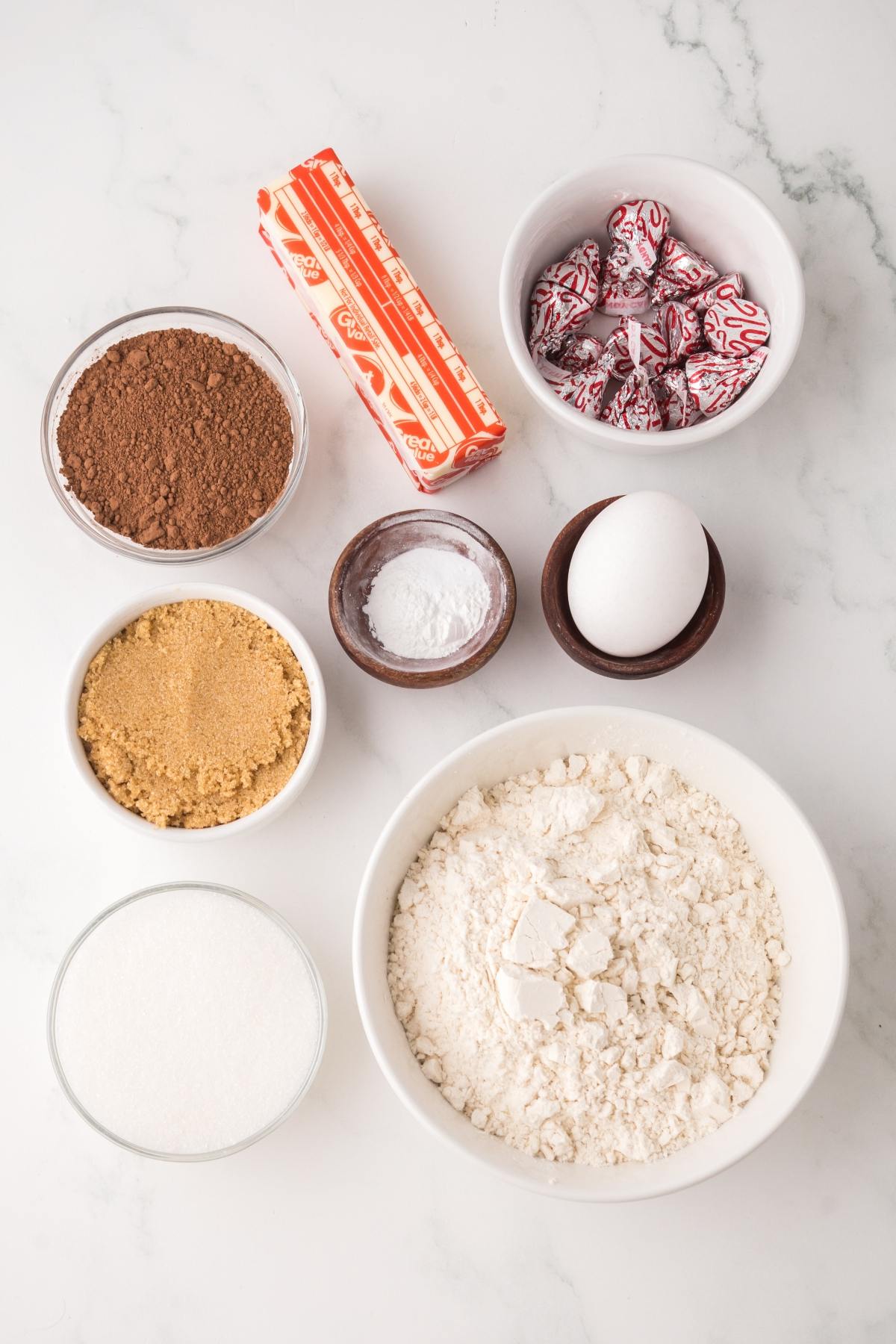 Baking ingredients in bowls: flour, sugar, brown sugar, cocoa, egg, baking soda, butter, and peppermint candies.