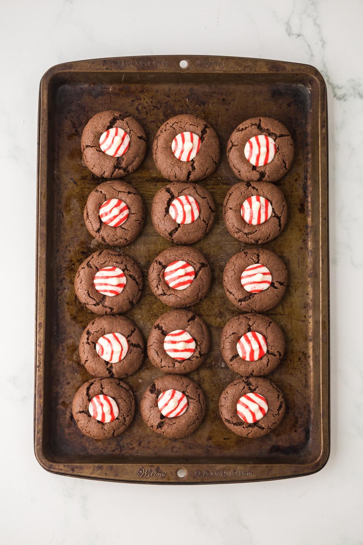 A baking sheet with 15 chocolate Peppermint kiss cookies topped with red and white striped candies.