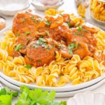 A plate of noodles topped with Salisbury Steak Meatballs in a mushroom sauce, garnished with chopped parsley.
