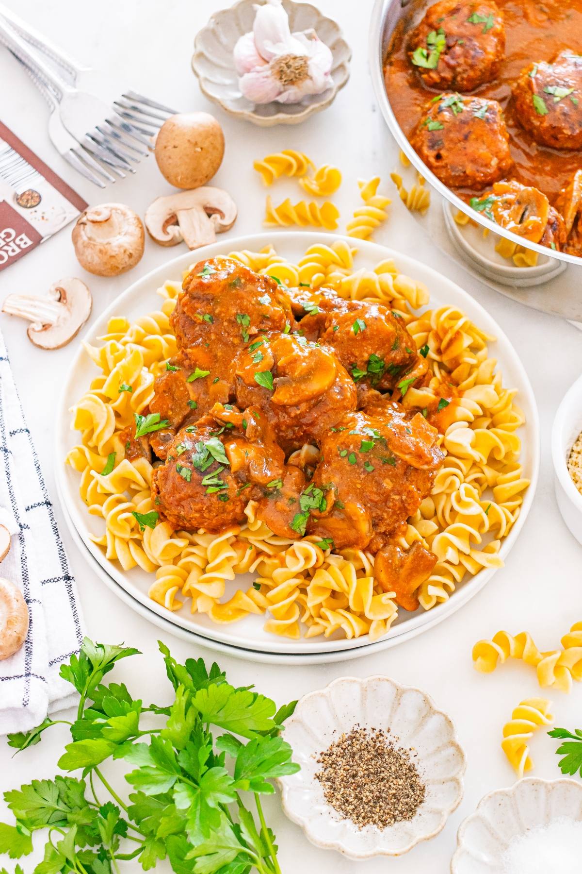 A plate of rotini pasta topped with saucy meatballs and mushrooms, garnished with chopped parsley.