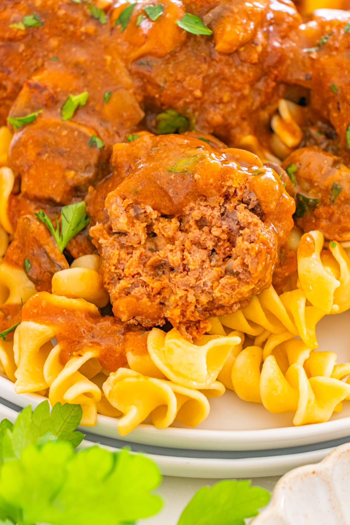 A sliced meatball with gravy served over egg noodles, garnished with chopped parsley.