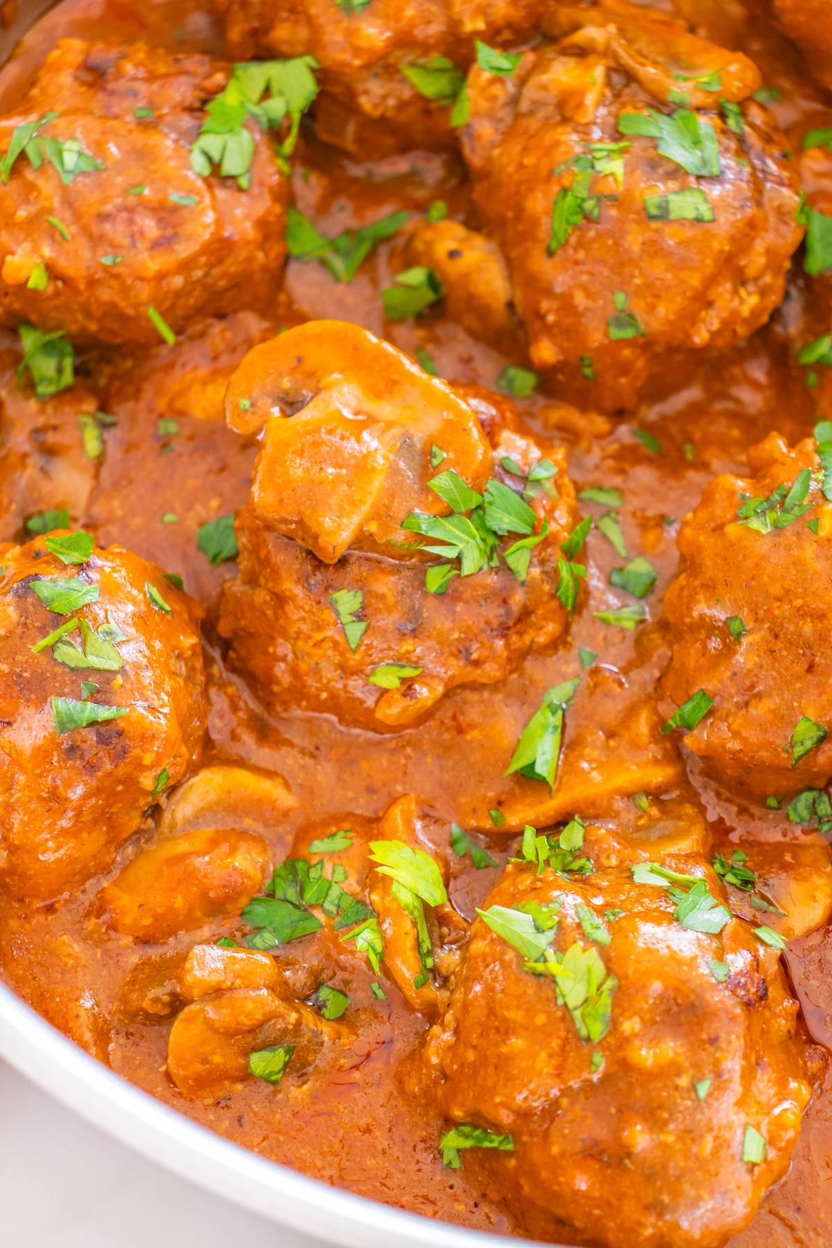 Meatballs in a rich red sauce with mushrooms, garnished with chopped fresh parsley.