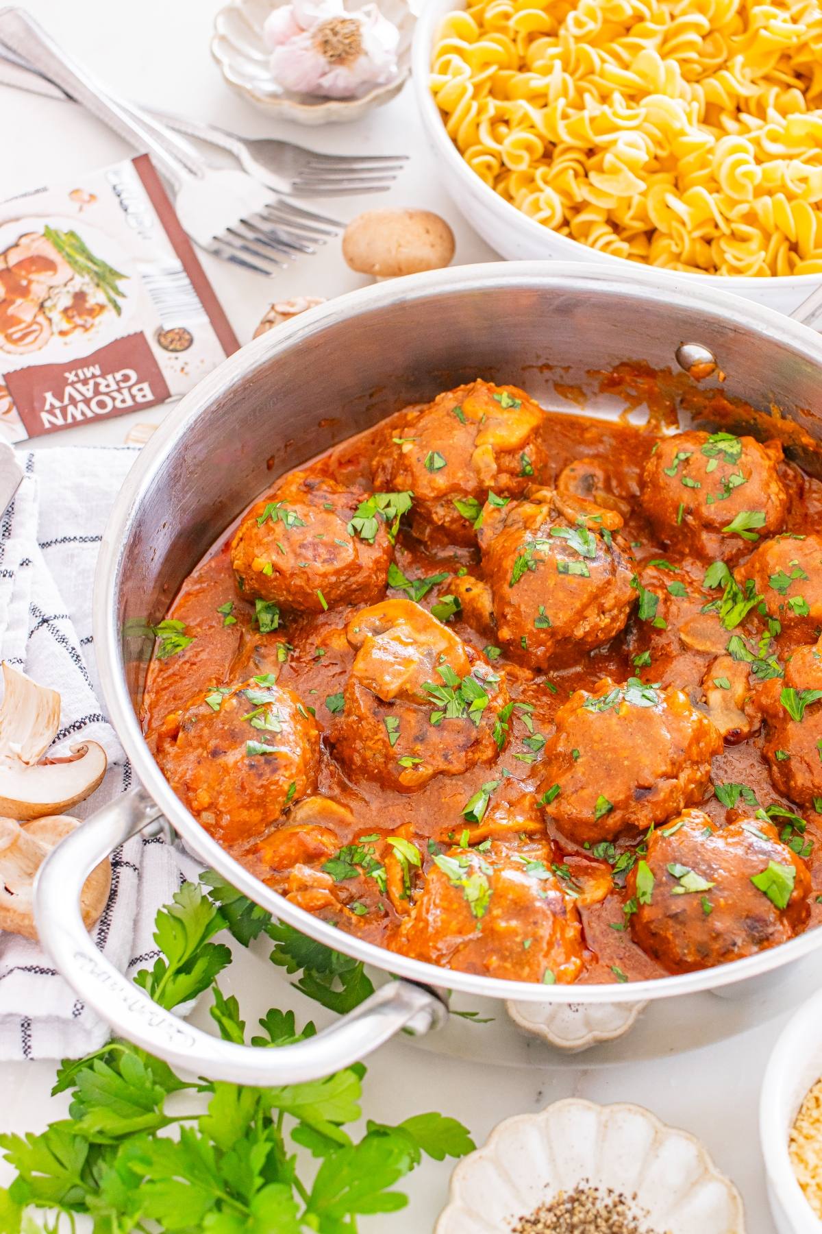 A pot of meatballs in tomato sauce, garnished with herbs, next to a bowl of cooked pasta.