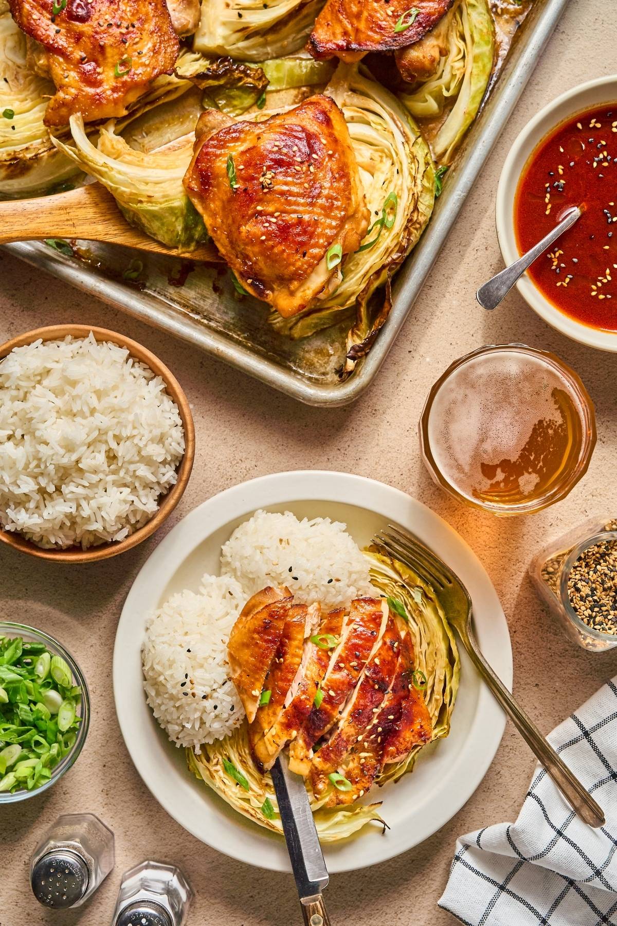 Plate with roasted chicken, steamed rice, cabbage, and sauce, alongside a tray of more chicken and rice bowls.