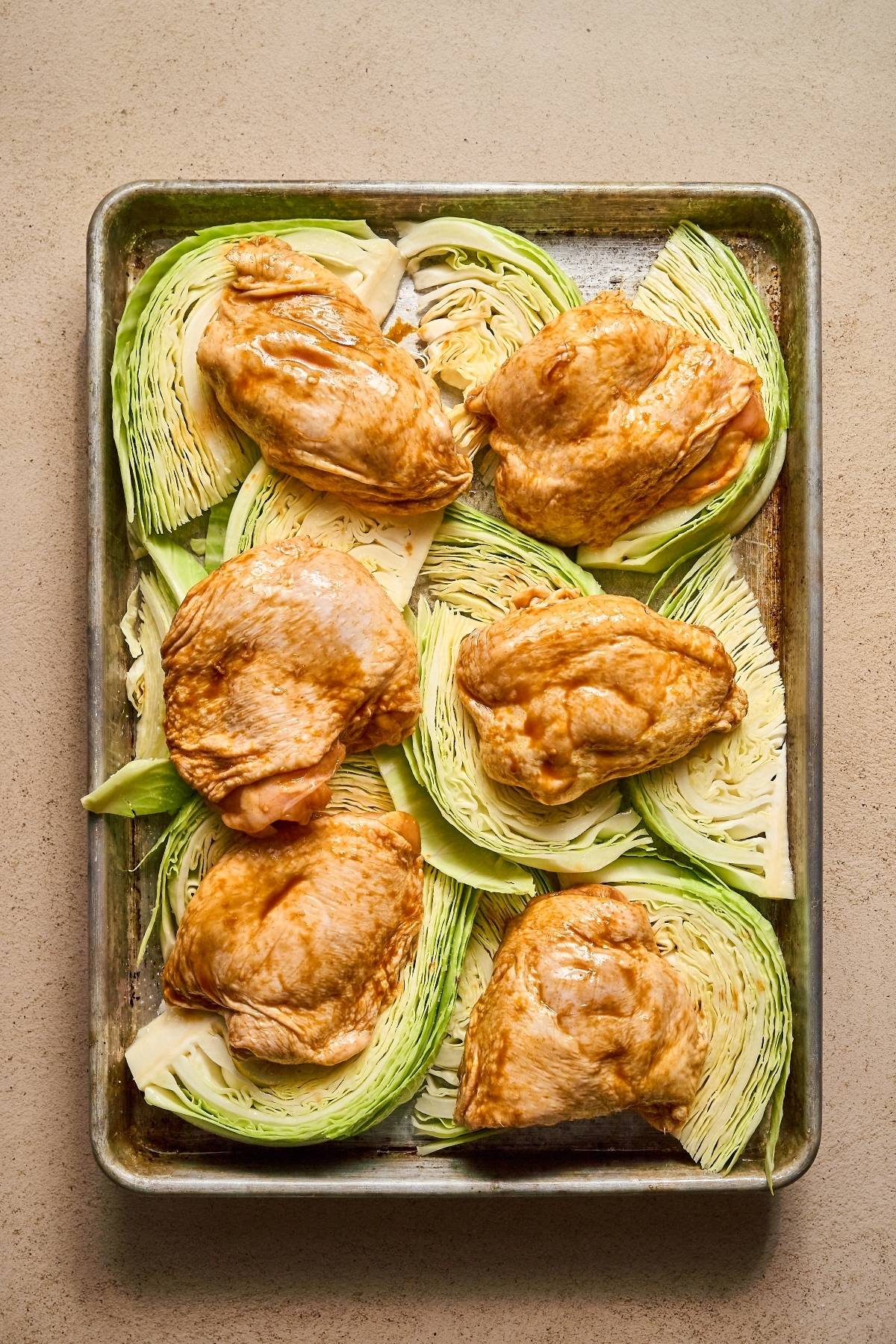 Raw seasoned chicken thighs arranged on cabbage wedges on a baking sheet, ready to be cooked.