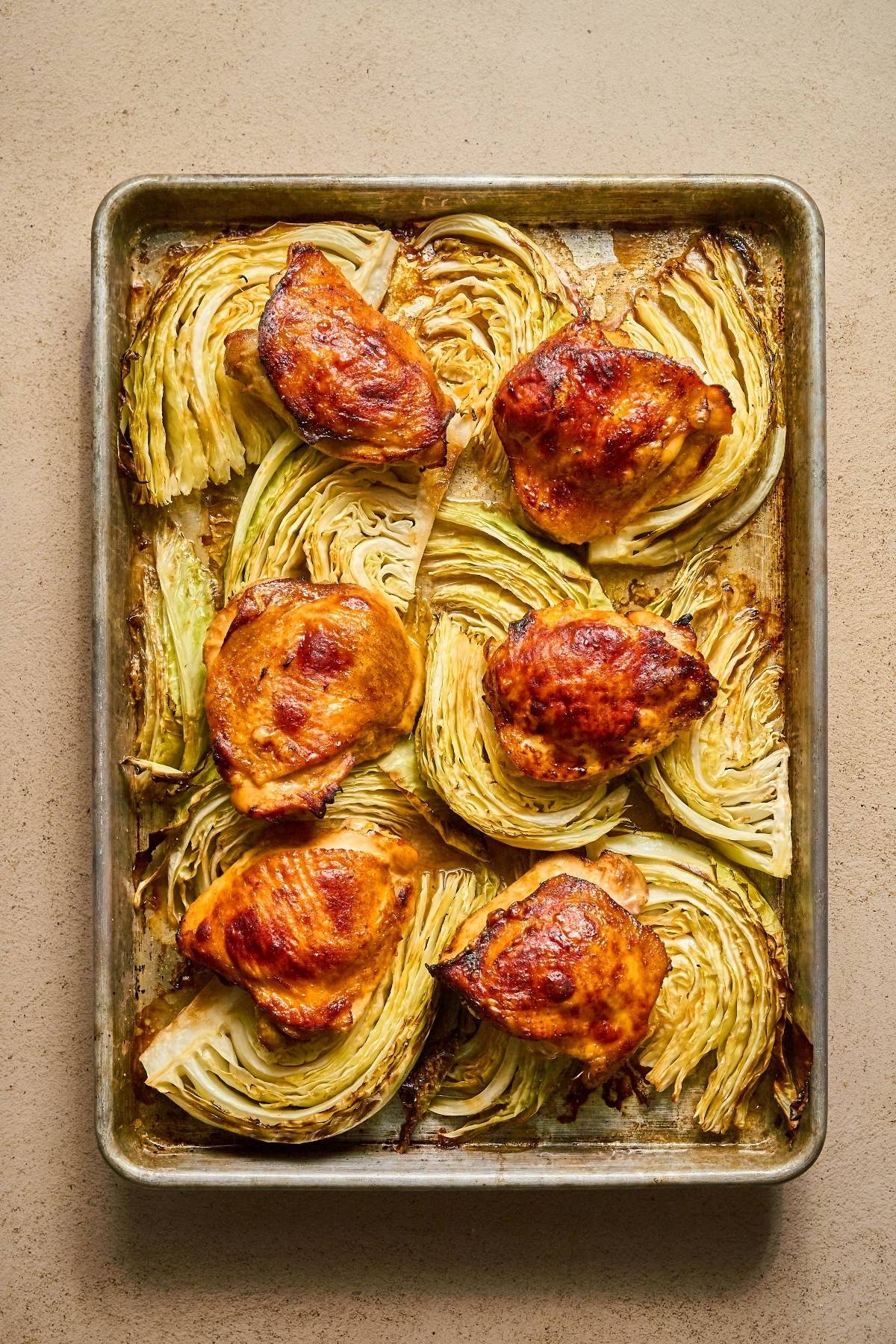 Roasted chicken thighs and cabbage wedges arranged on a baking sheet.