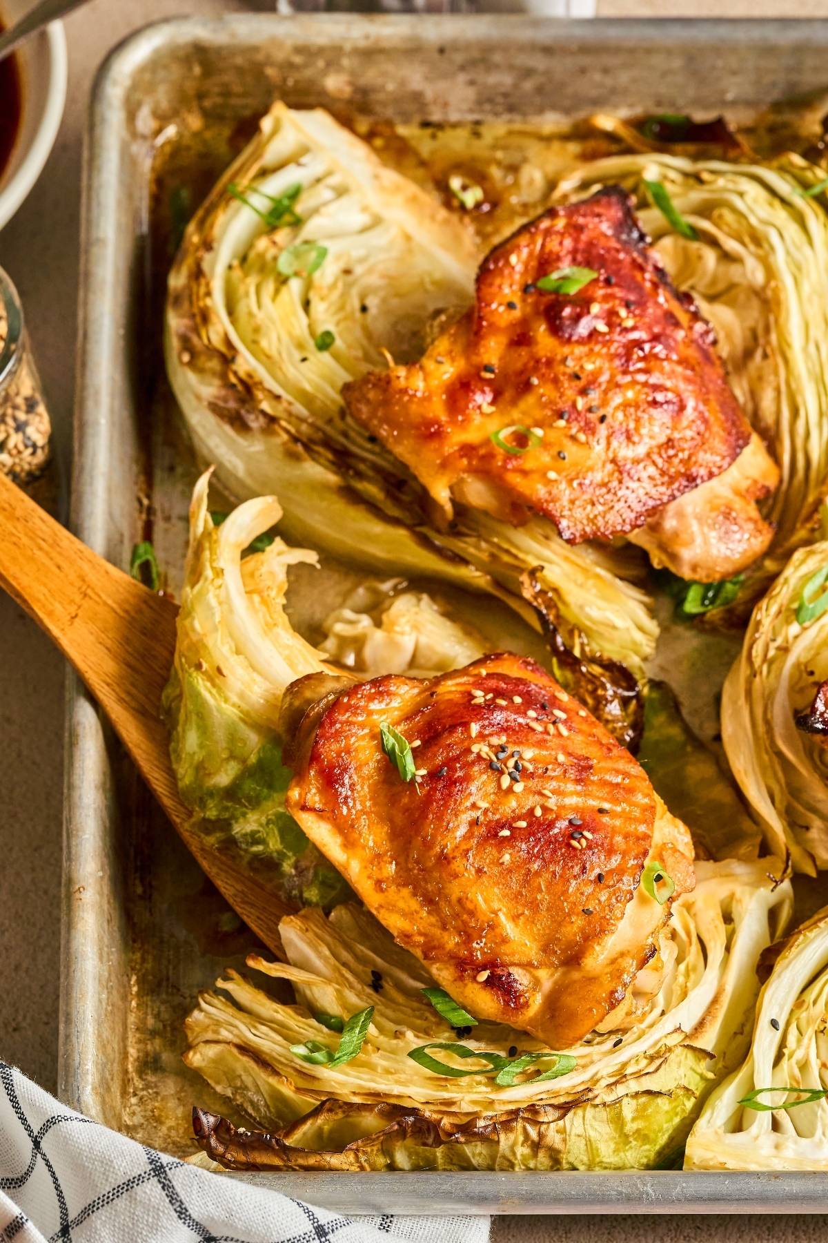 Roasted chicken thighs and cabbage wedges on a baking sheet, garnished with chopped green onions.