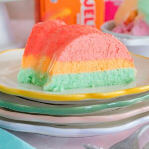 A slice of colorful Sherbet Layered Jello Mold sits on a stack of plates with forks beside it.