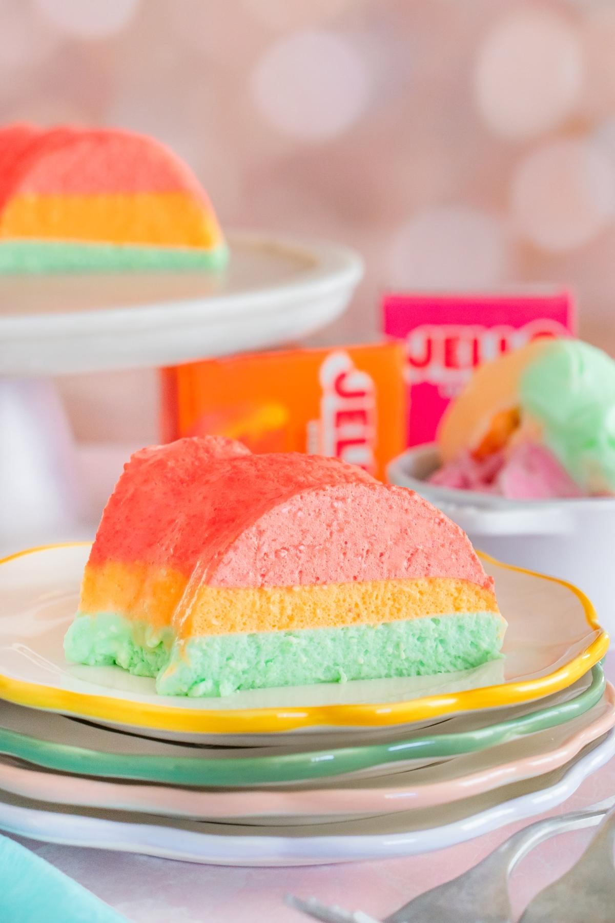 A slice of colorful layered Jello dessert on a plate, with pastel pink, yellow, and green layers.