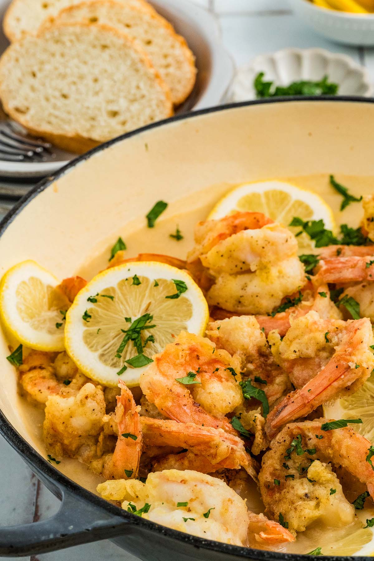Shrimp Francese in a creamy sauce garnished with lemon slices and parsley, served with slices of bread.