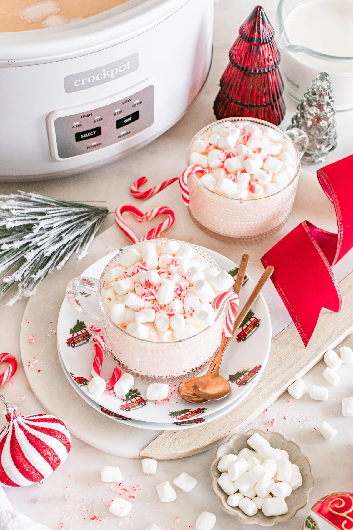 Two mugs of hot chocolate with marshmallows and peppermint, surrounded by festive holiday decorations.