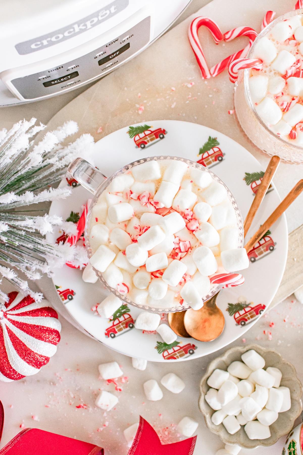 A cup of hot chocolate with marshmallows and crushed candy canes, surrounded by festive holiday decor.