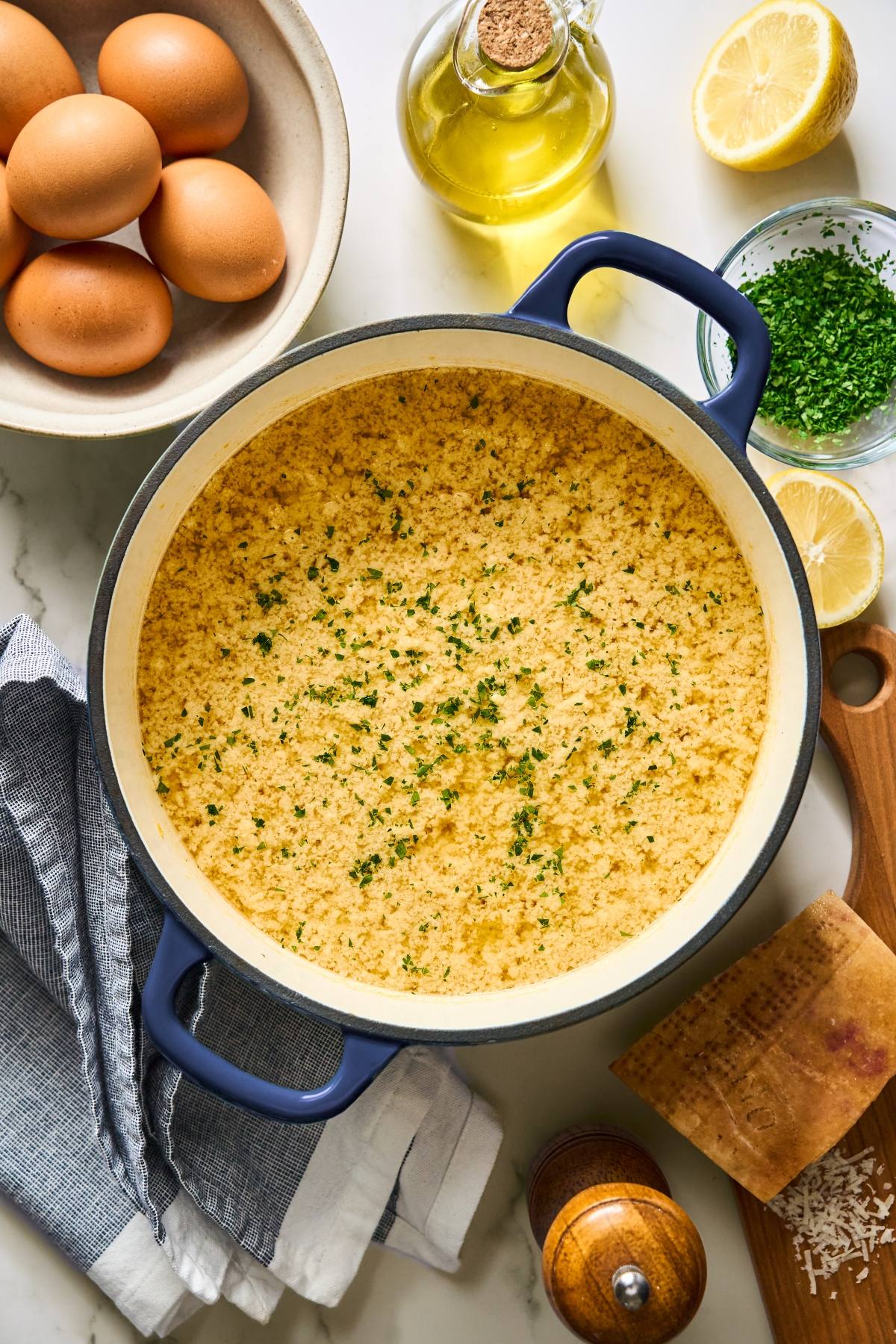 A pot of cooked polenta garnished with herbs, surrounded by eggs, cheese, lemon, oil, and chives.