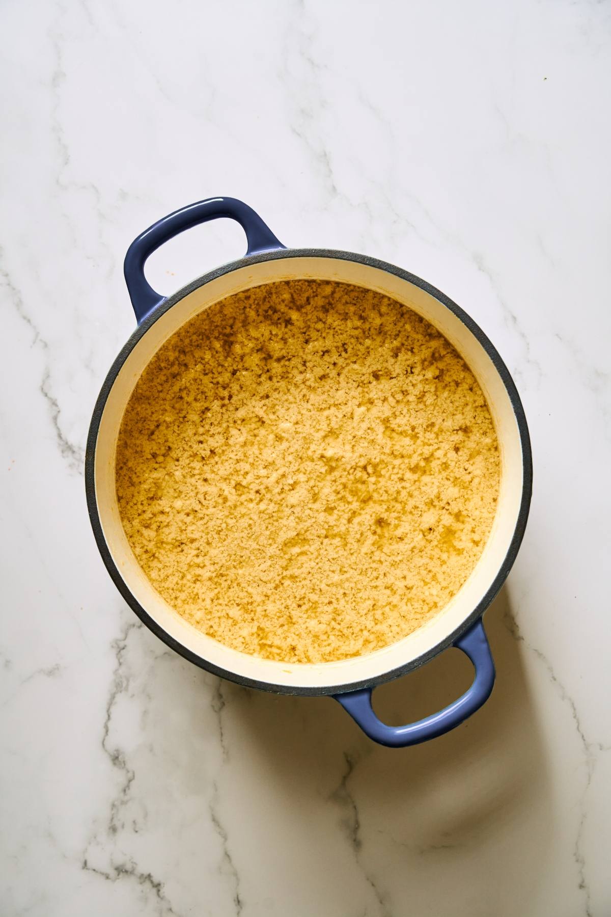 A large blue pot filled with crumbled cornbread sits on a white marble surface.