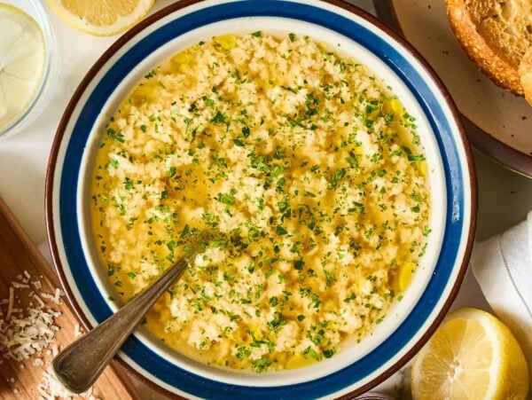 A bowl of garlic spread topped with herbs and olive oil, surrounded by bread, lemon, and grated cheese—perfect as a starter alongside Stracciatella Soup.