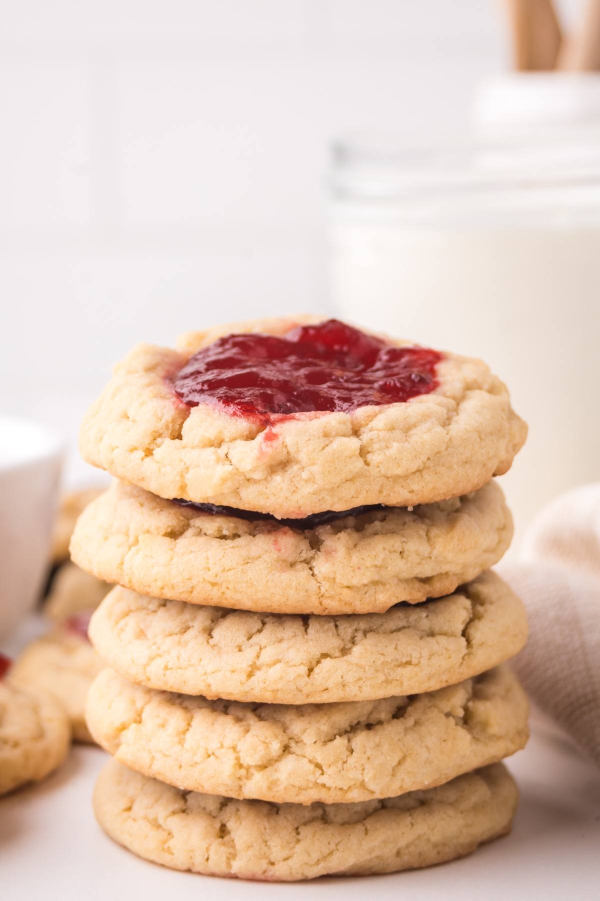 A stack of cookies topped with red jam, with a glass of milk in the background.