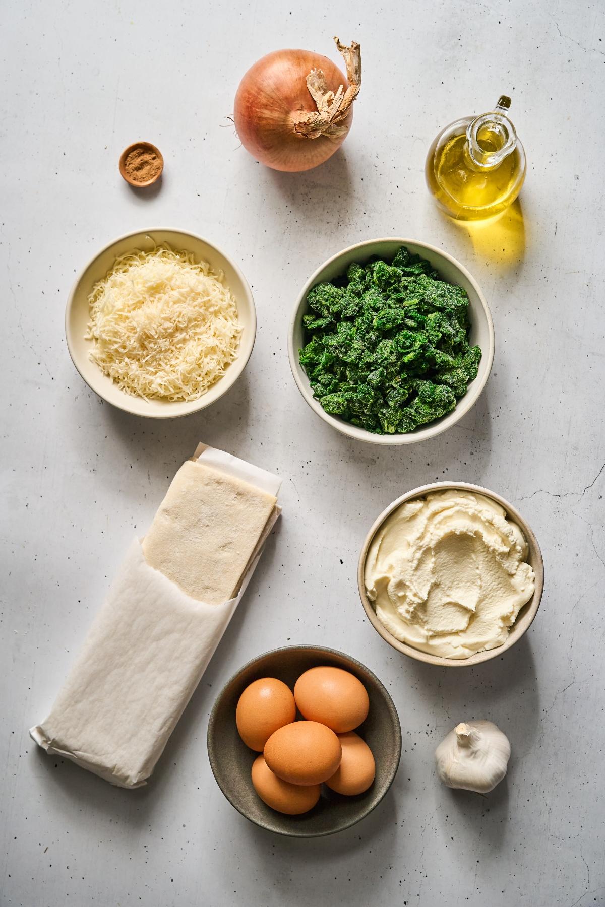 Ingredients for cooking: onion, olive oil, spinach, ricotta, eggs, garlic, lasagna sheets, cheese, and nutmeg.