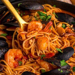 Frutti di Mare spaghetti with mussels, shrimp, and tomato sauce, garnished with parsley in a skillet with a serving spoon.