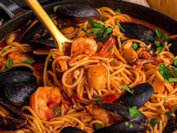 Frutti di Mare spaghetti with mussels, shrimp, and tomato sauce, garnished with parsley in a skillet with a serving spoon.
