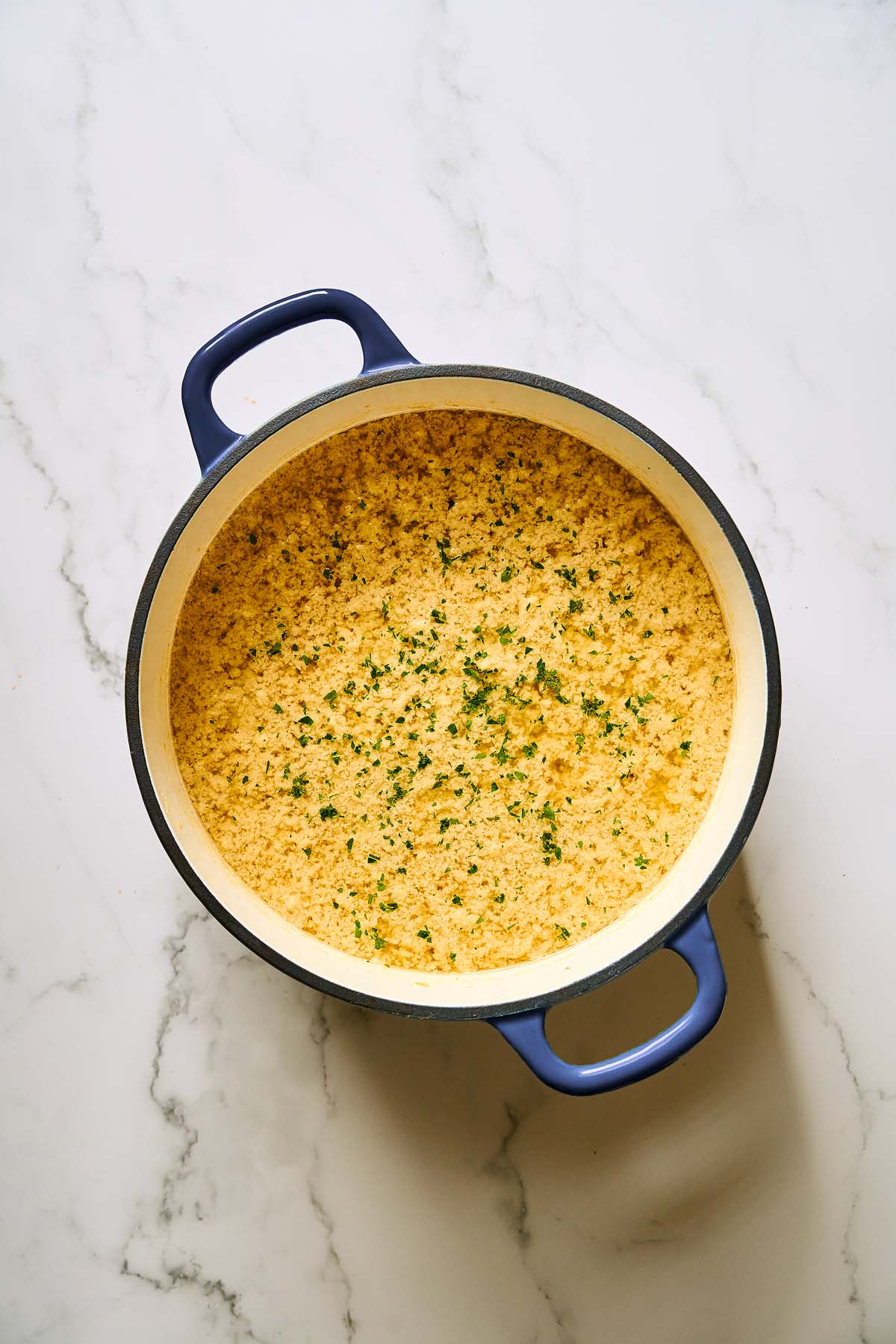 A blue pot filled with Stracciatella Soup, garnished with chopped herbs on a marble surface.