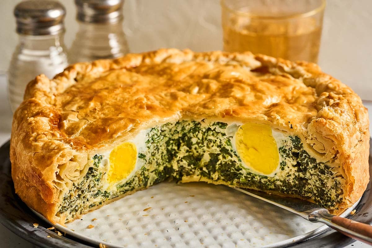 A savory Torta Pasqualina with golden crust, filled with spinach and whole boiled eggs, with a slice cut out.