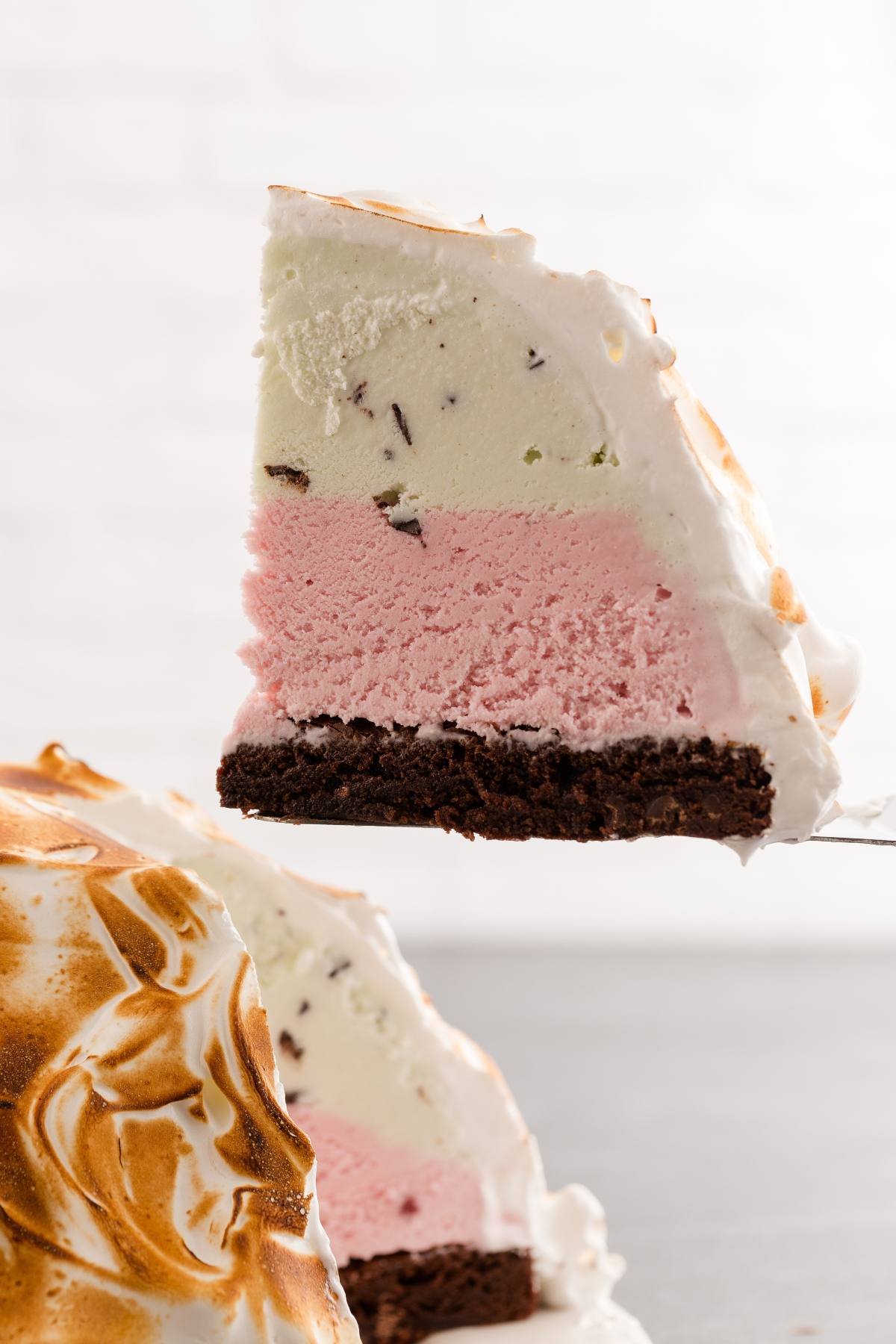 A slice of baked Alaska with layers of cake, pink and white ice cream, and toasted meringue.