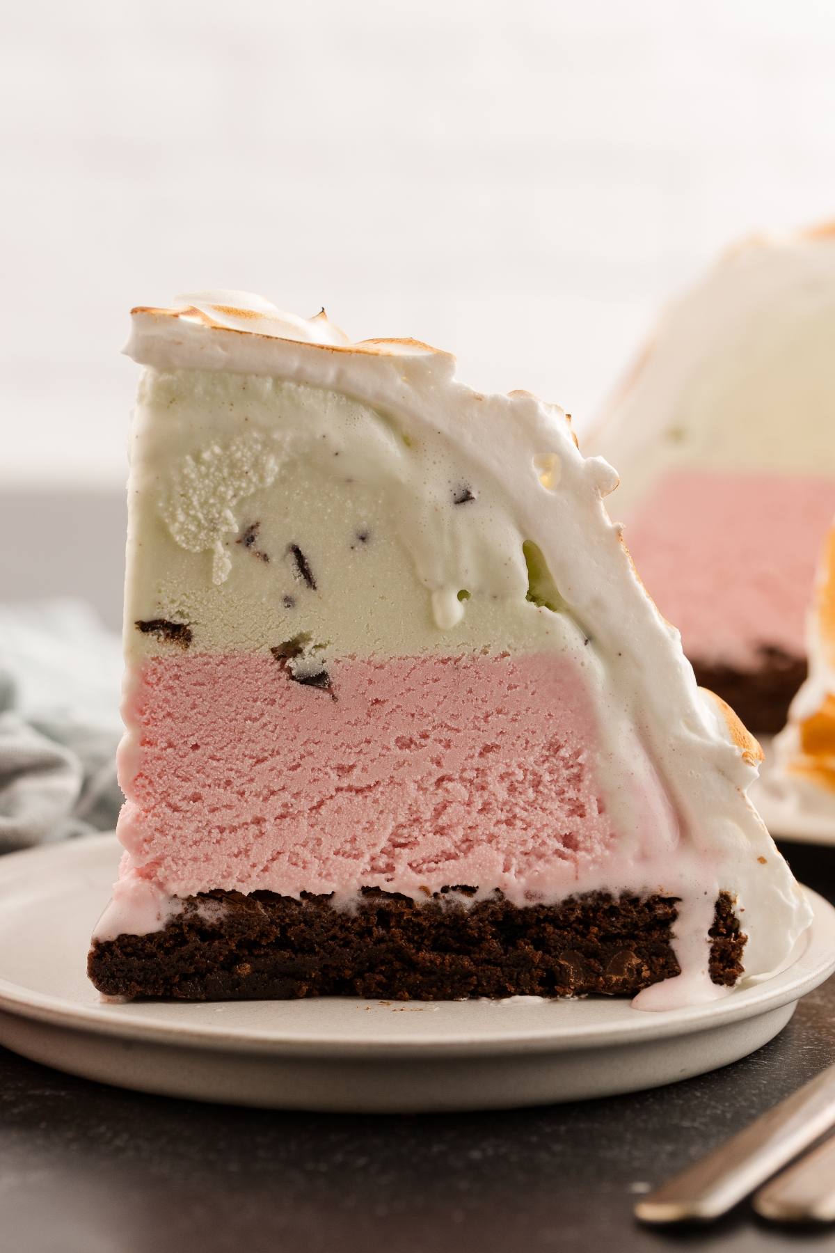 Slice of baked Alaska with layers of chocolate, strawberry, and pistachio ice cream, topped with toasted meringue.