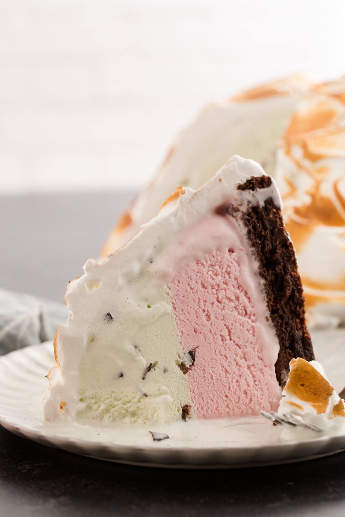 A slice of baked Alaska with chocolate and vanilla cake, strawberry and mint ice cream, and toasted meringue.