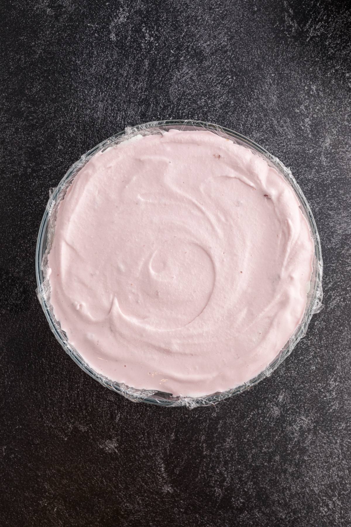 A round dish filled with smooth, light pink mousse on a dark textured surface.