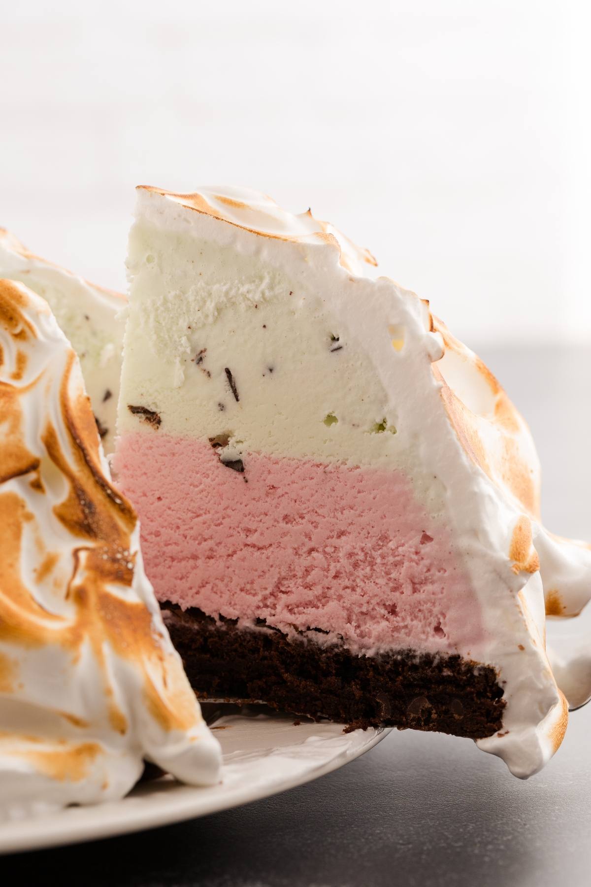Slice of baked Alaska with layers of chocolate cake, strawberry and vanilla ice cream, topped with toasted meringue.