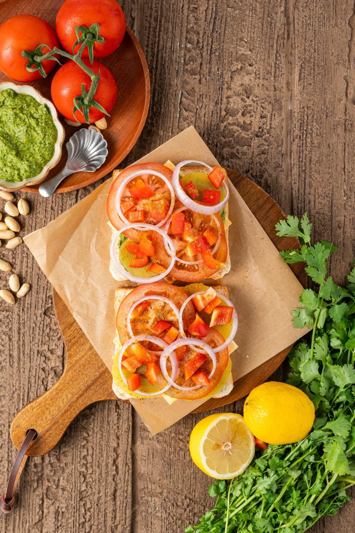 Open-faced veggie sandwiches with tomato, onion, and bell pepper on bread, surrounded by fresh ingredients.
