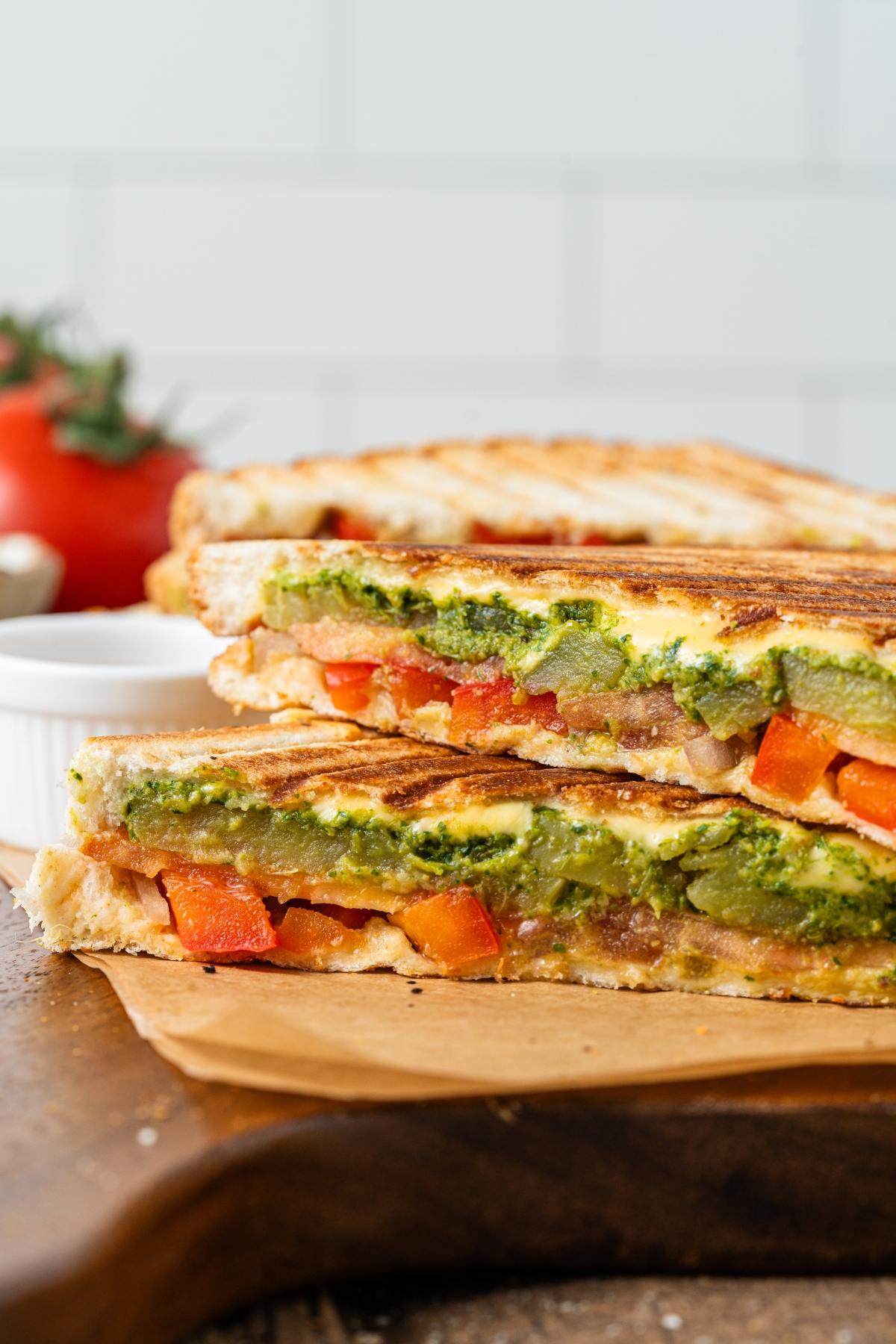 A grilled vegetable and cheese sandwich cut in half, showing layers of tomato, pepper, and pesto.
