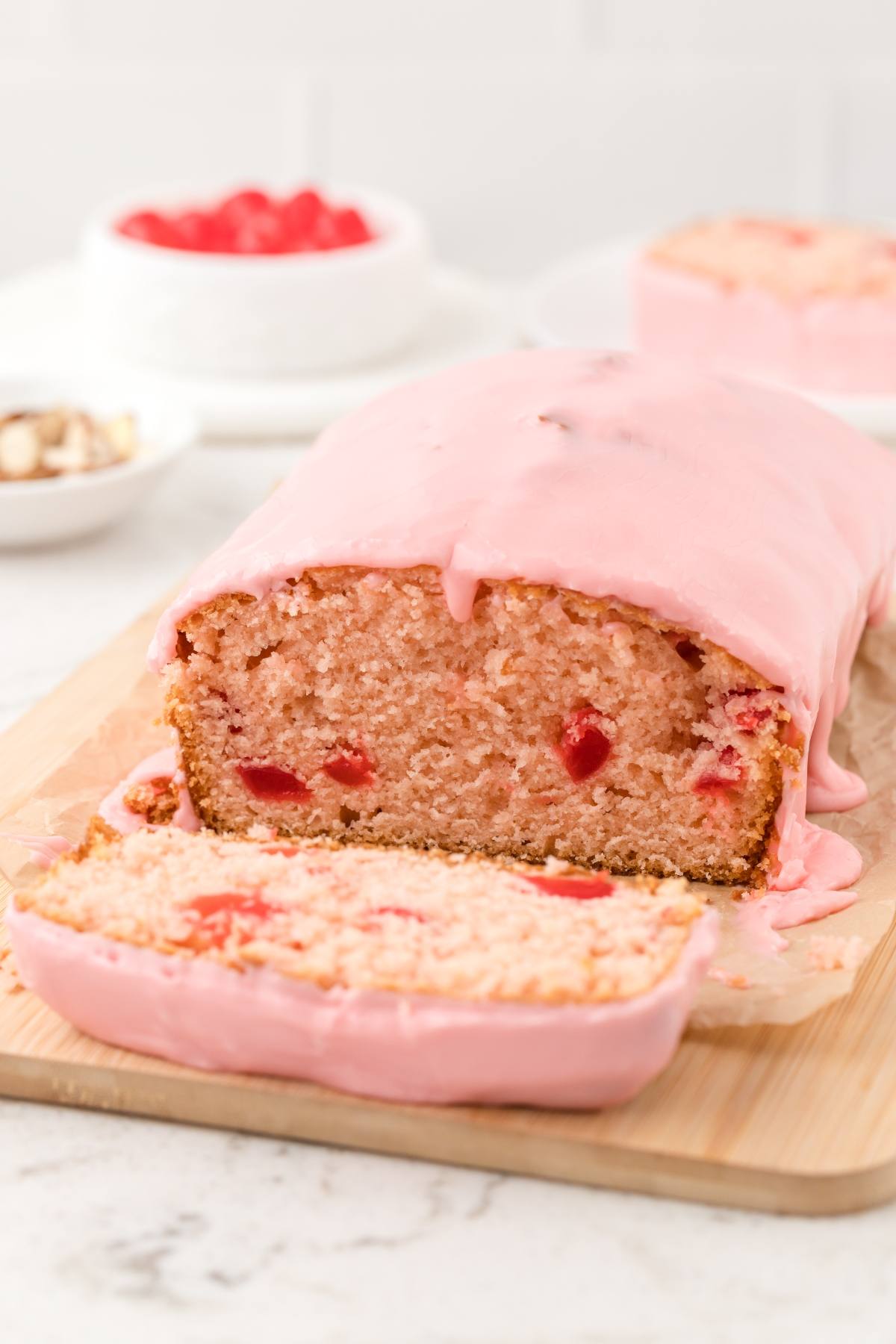 A sliced loaf of pink cherry bread with pink icing on a wooden board.