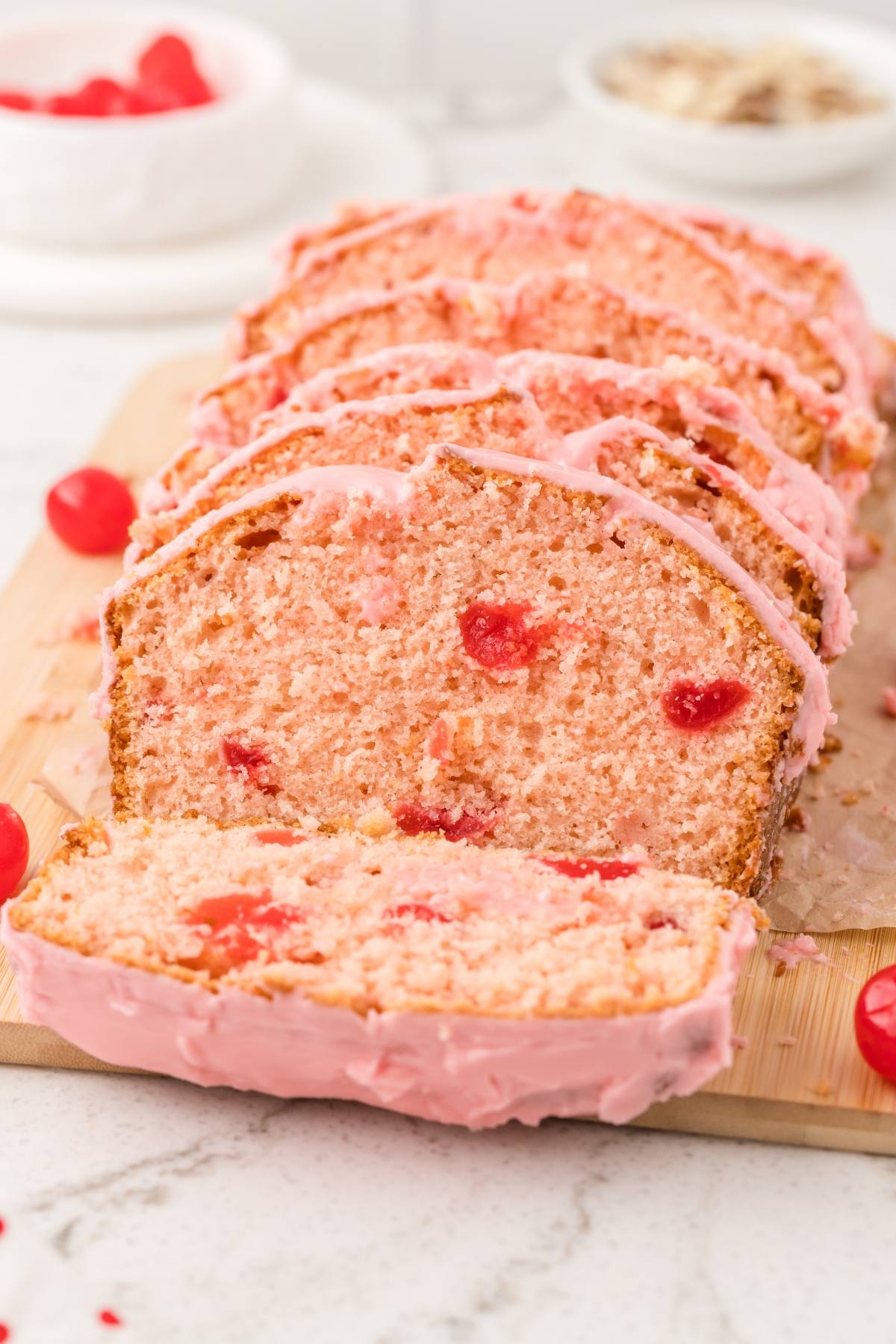 Sliced cherry bread with pink icing and visible cherry pieces on a wooden board.