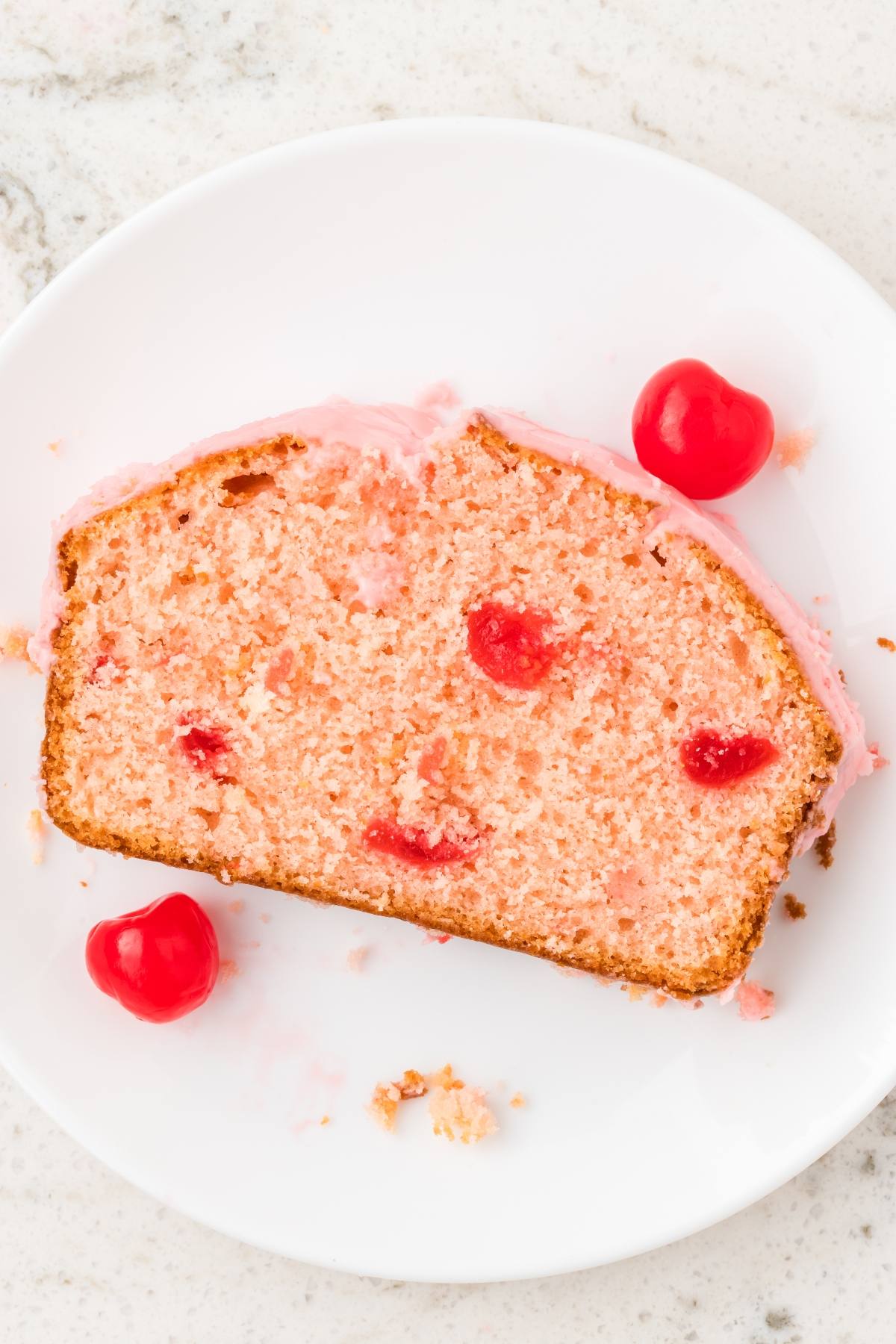 A slice of pink cherry bread with cherries on a white plate, topped with pink icing.