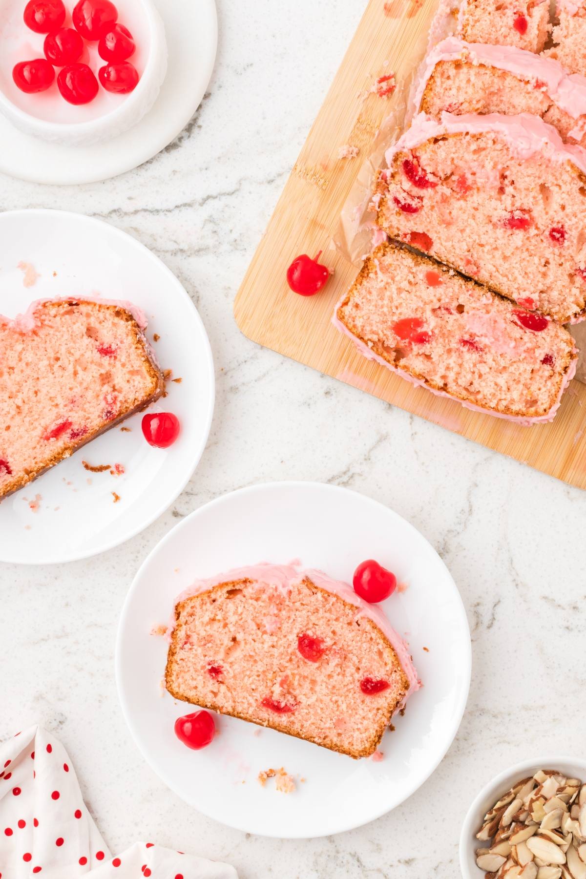 Sliced cherry bread with pink icing on plates and a cutting board, topped with maraschino cherries.