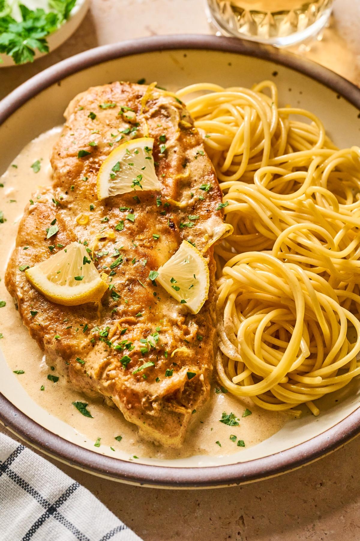 Chicken breast with lemon slices in creamy sauce, served with plain spaghetti on a plate.